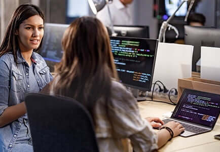 two female software developers discussing an idea in front of their computers